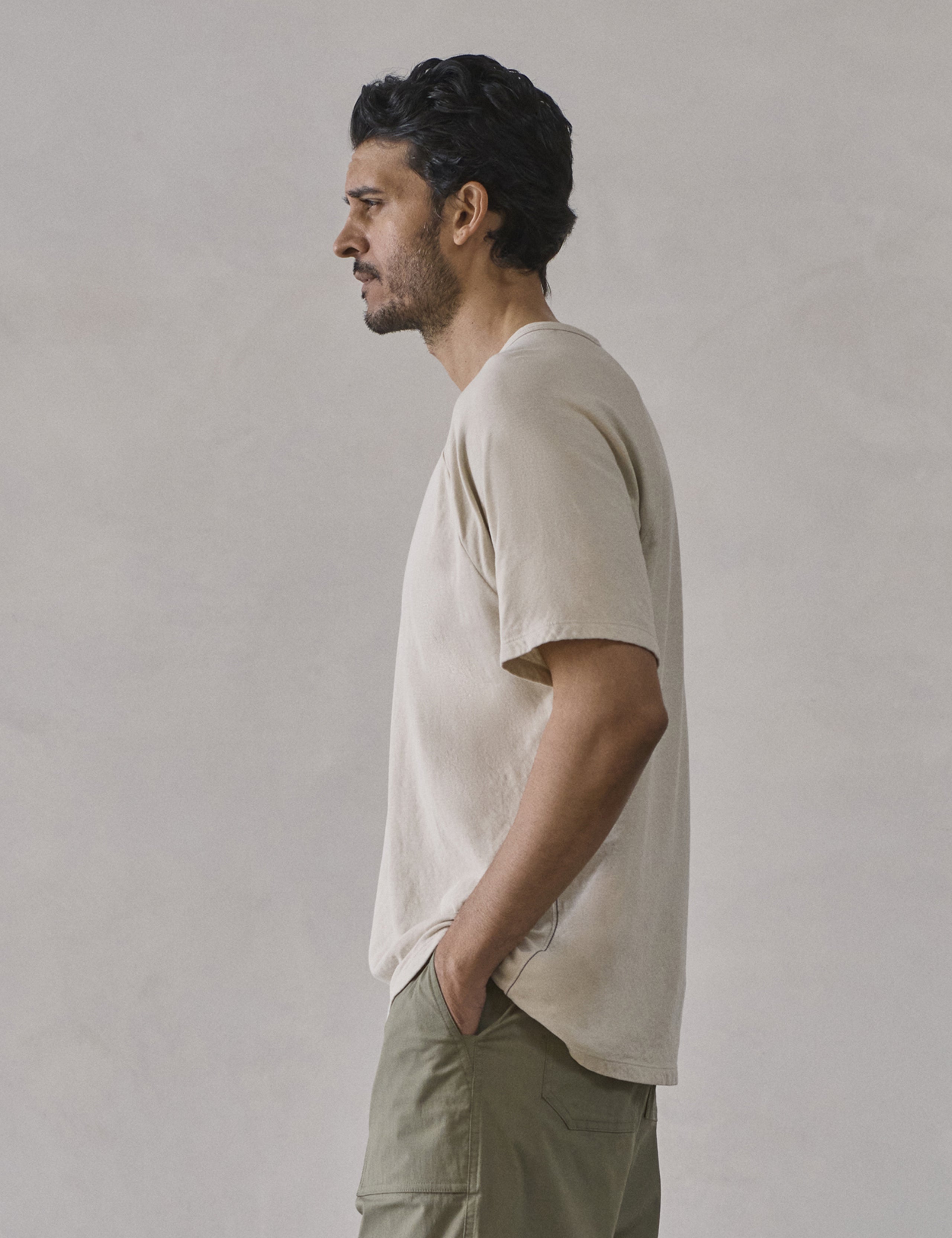 Left side profile upper-body view of man wearing Buckhorn Cotton Raglan Tee 2.0 in Bone white from AETHER Apparel.