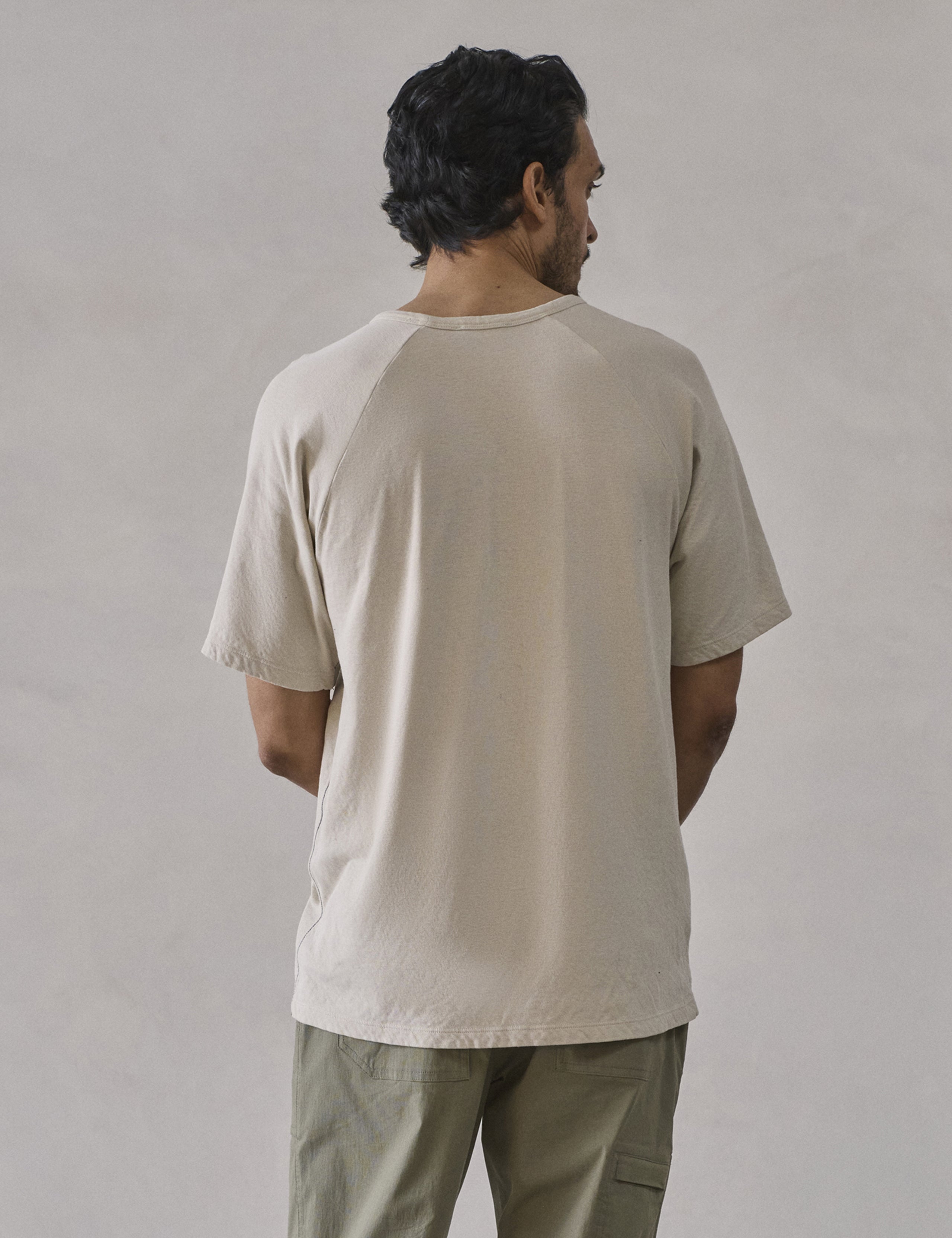 Rear upper-body view of man wearing Buckhorn Cotton Raglan Tee 2.0 in Bone white from AETHER Apparel.