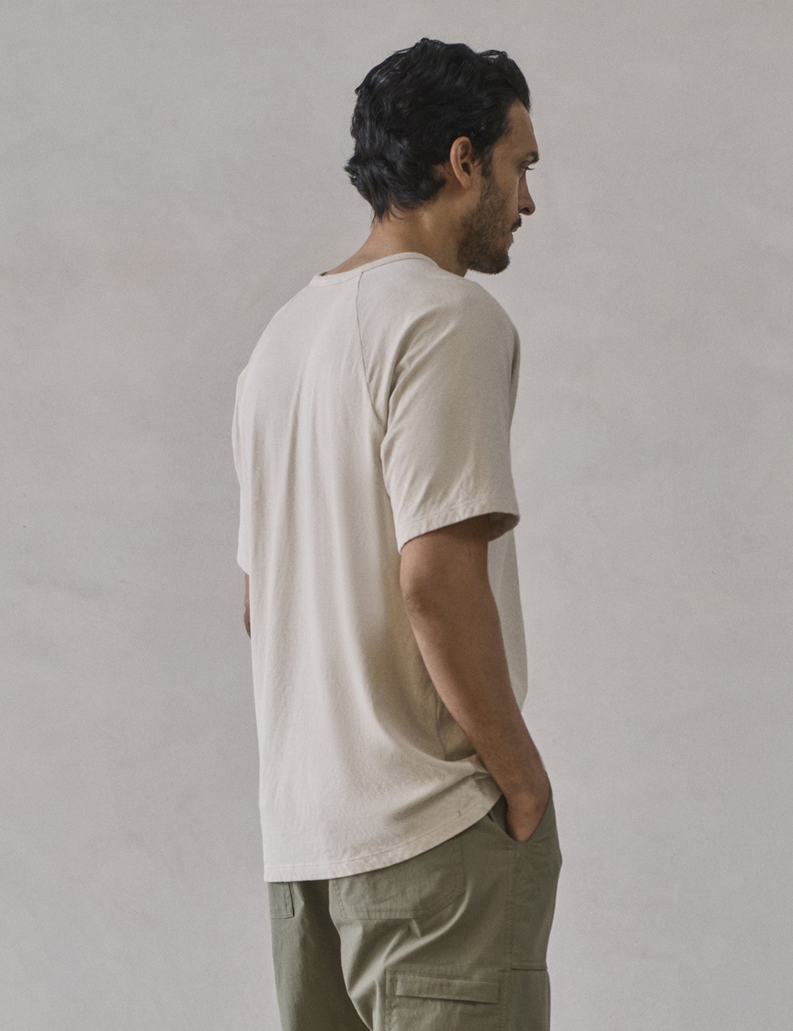 Rear 3/4 upper-body view of man wearing Buckhorn Cotton Raglan Tee 2.0 in Bone white from AETHER Apparel.