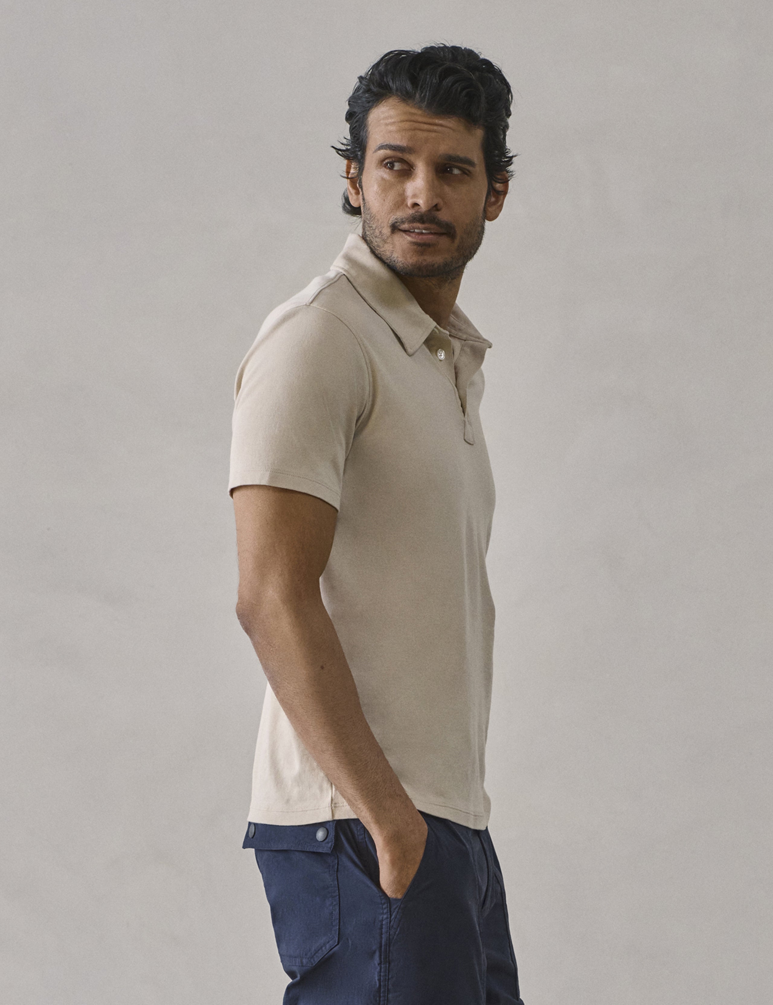 Side profile view of man wearing Emery Pima Polo in Bone white from AETHER Apparel.