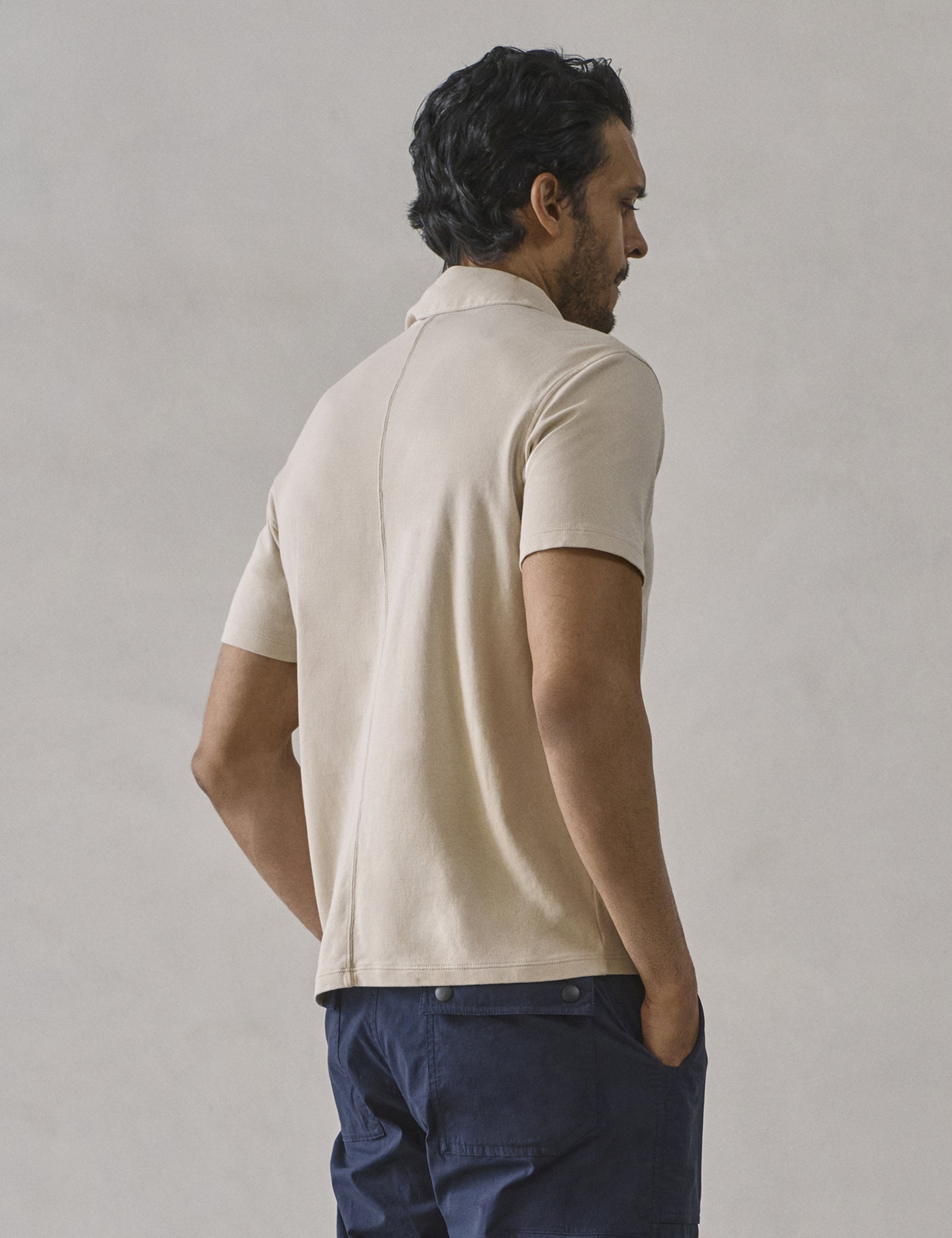 Rear 3/4 body view of man wearing Emery Pima Polo in Bone white from AETHER Apparel.