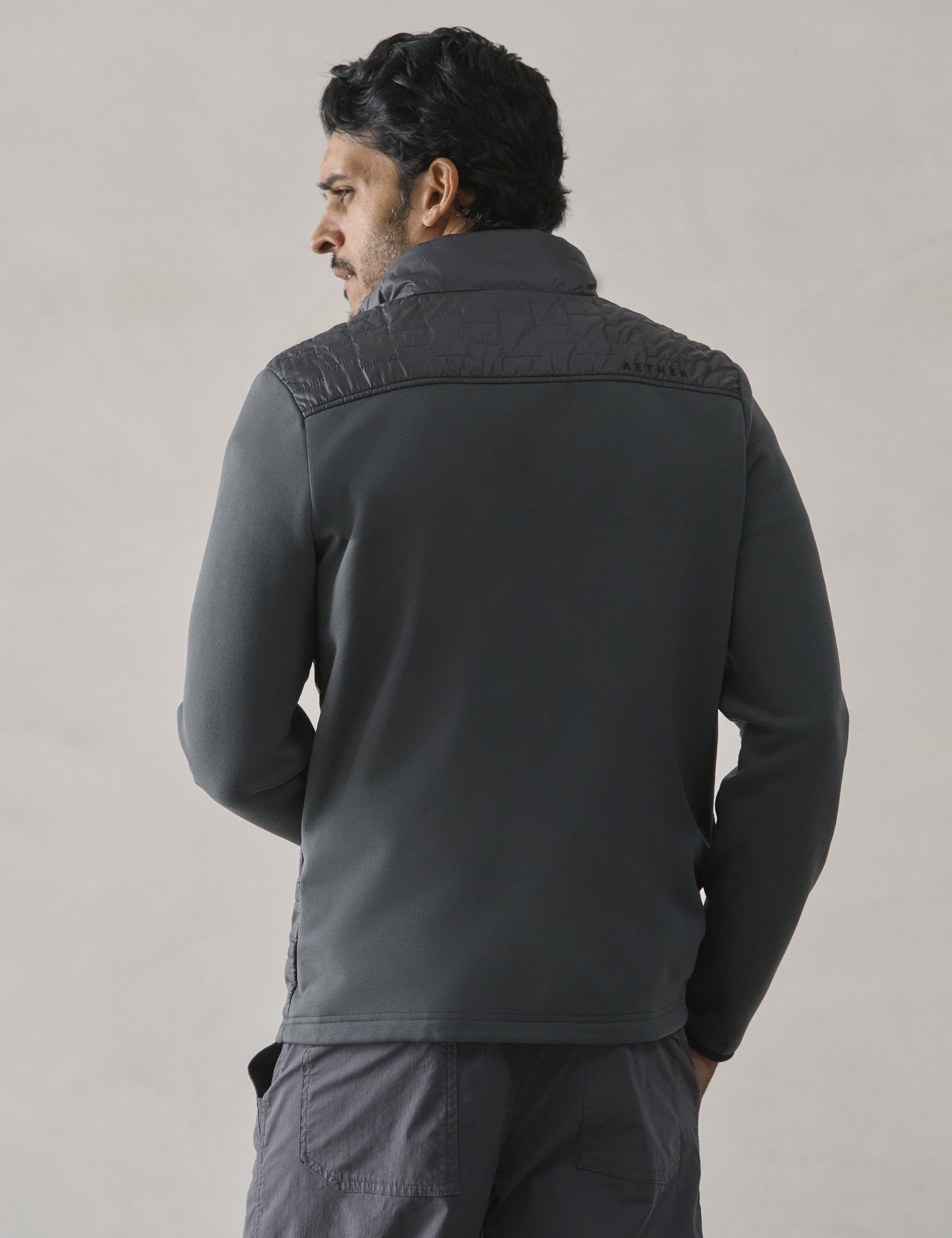 Rear view of man wearing Hybrid Tech Full-Zip in Graphite from AETHER Apparel.
