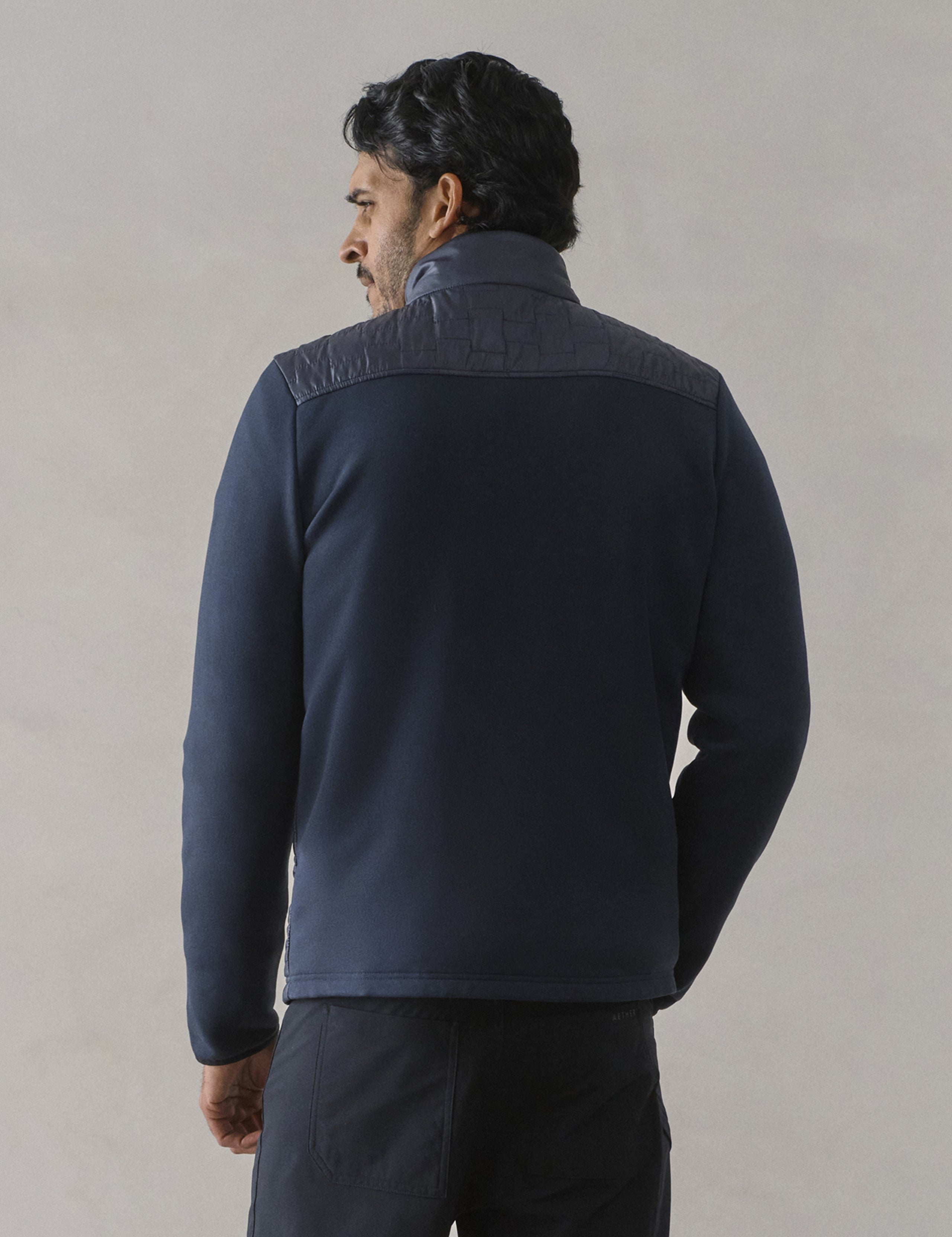 Rear view of man wearing Hybrid Tech Full-Zip in Total Eclipse dark blue from AETHER Apparel.