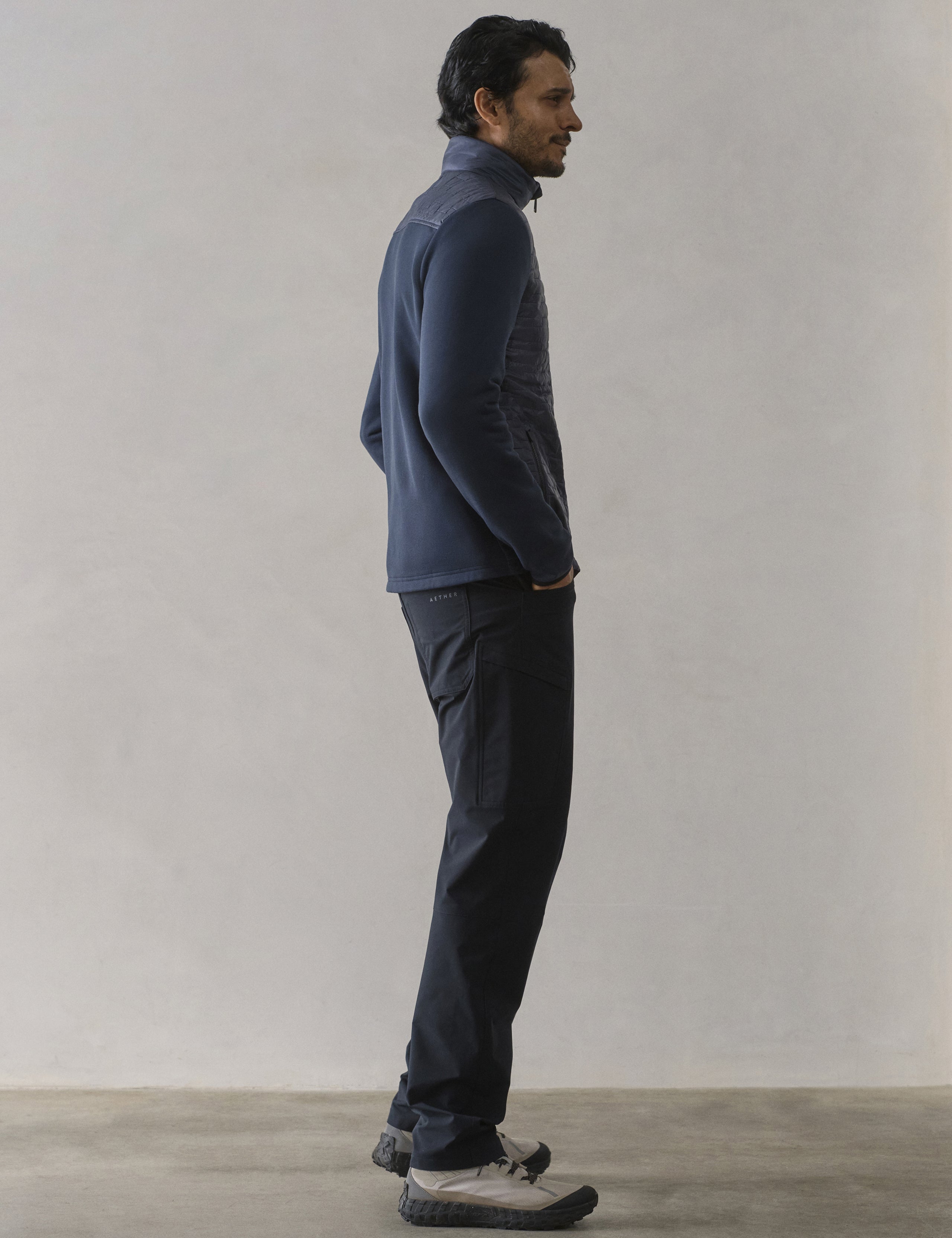 Side profile full-body view of man wearing Hybrid Tech Full-Zip in Total Eclipse dark blue from AETHER Apparel.