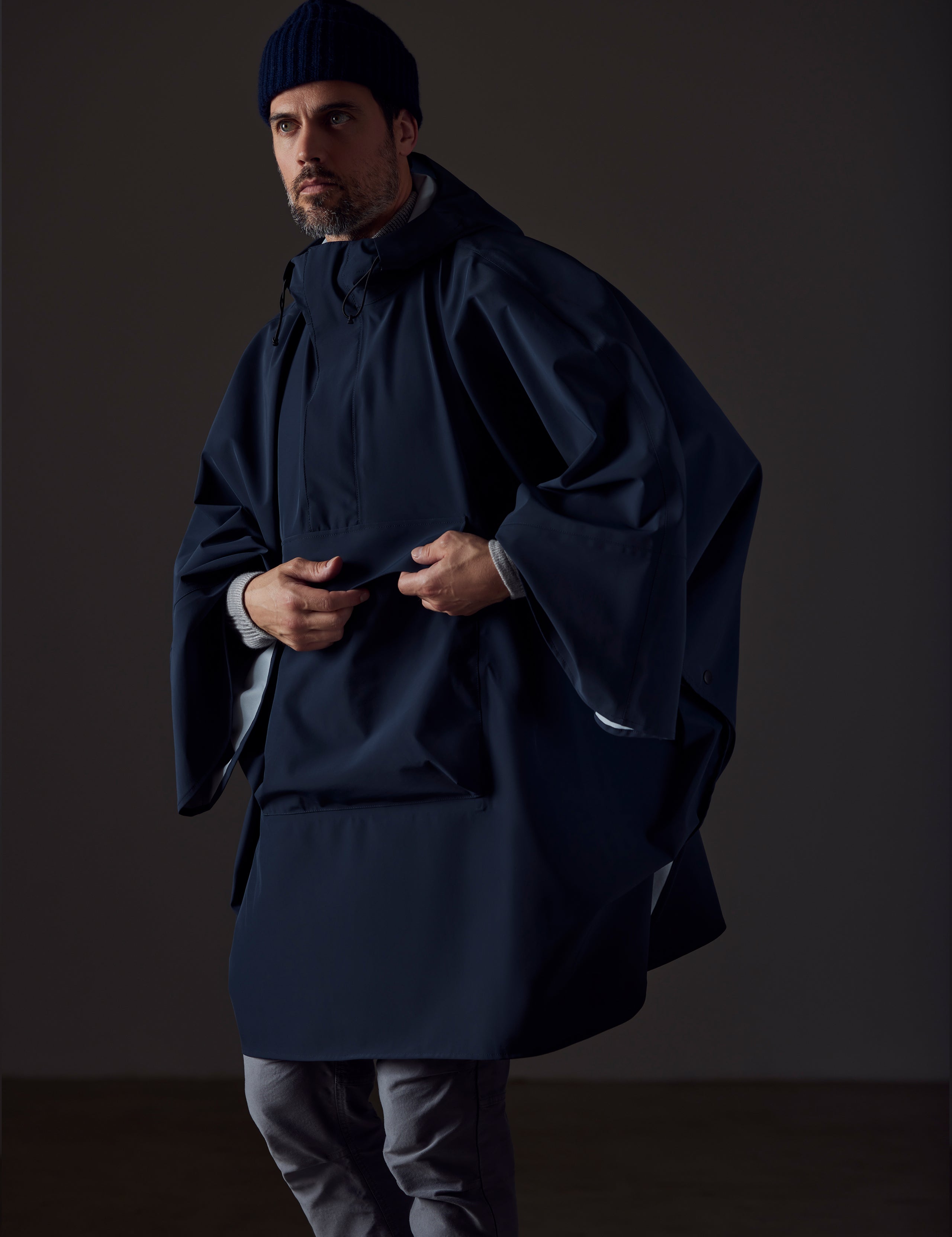 Front angled view of man wearing blue Line Poncho from AETHER Apparel, highlighting front drop pocket.