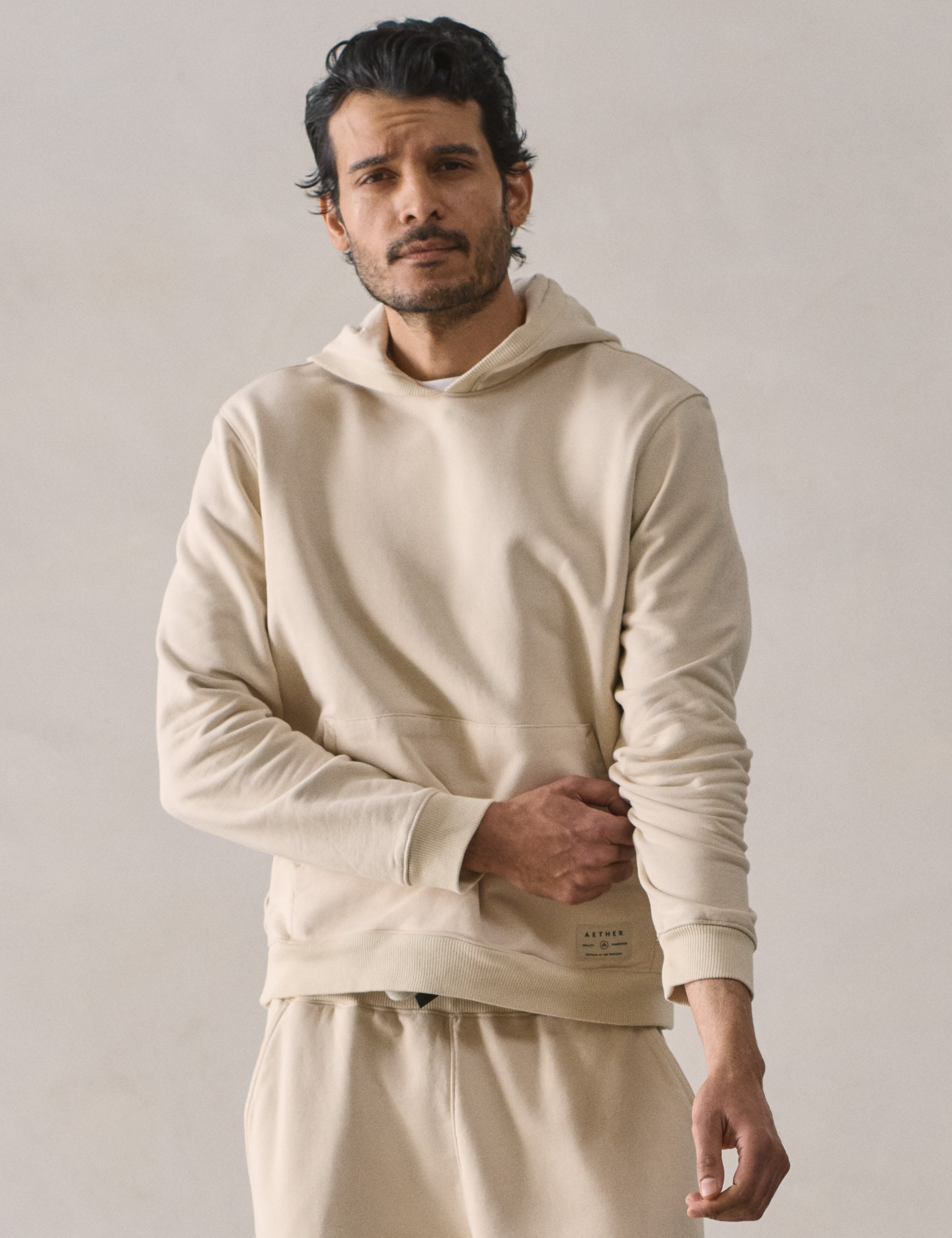 Front upper body view of man wearing Osa Pullover Hoodie in Bone white from AETHER Apparel.