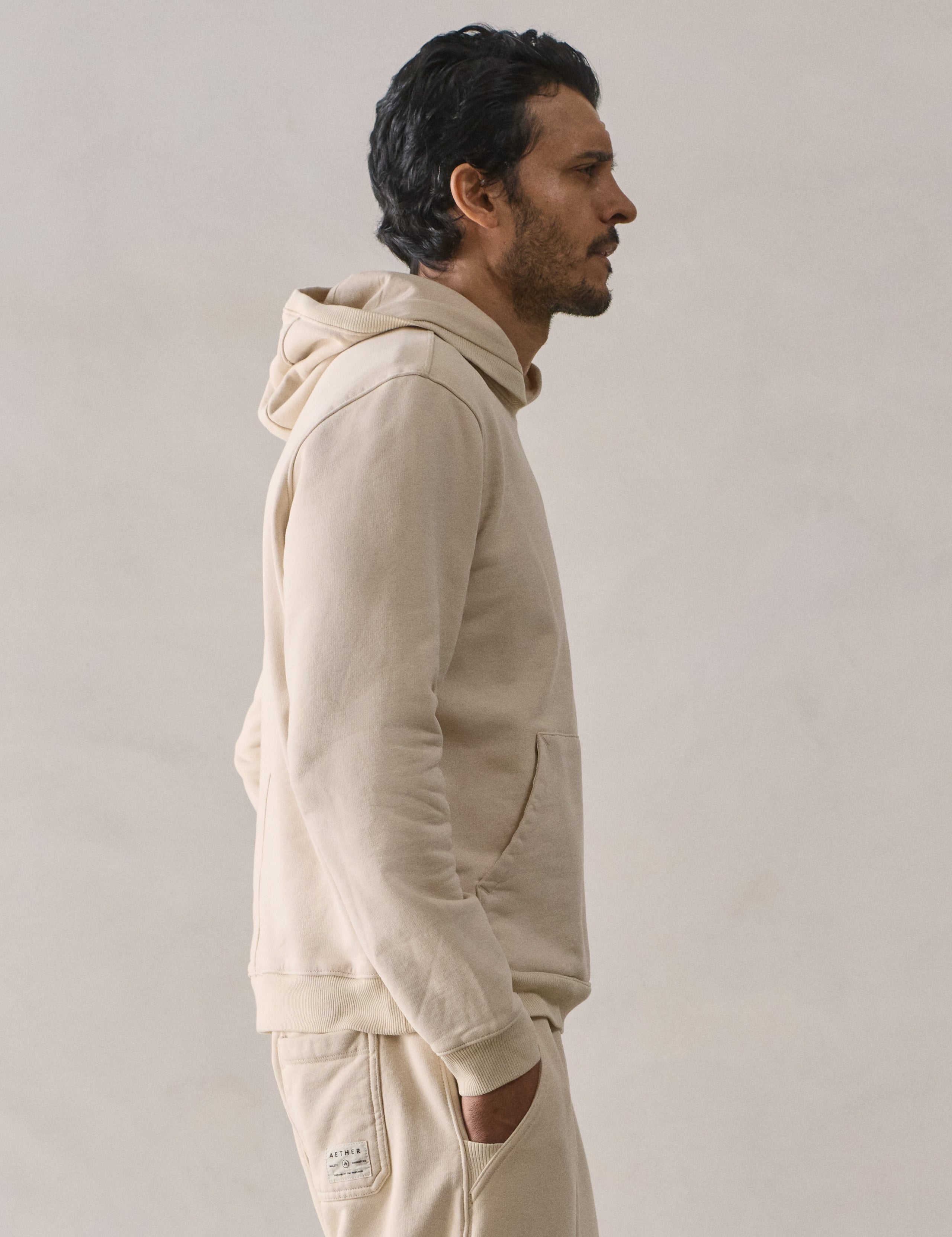 Right side upper body profile view of man wearing Osa Pullover Hoodie in Bone white from AETHER Apparel.