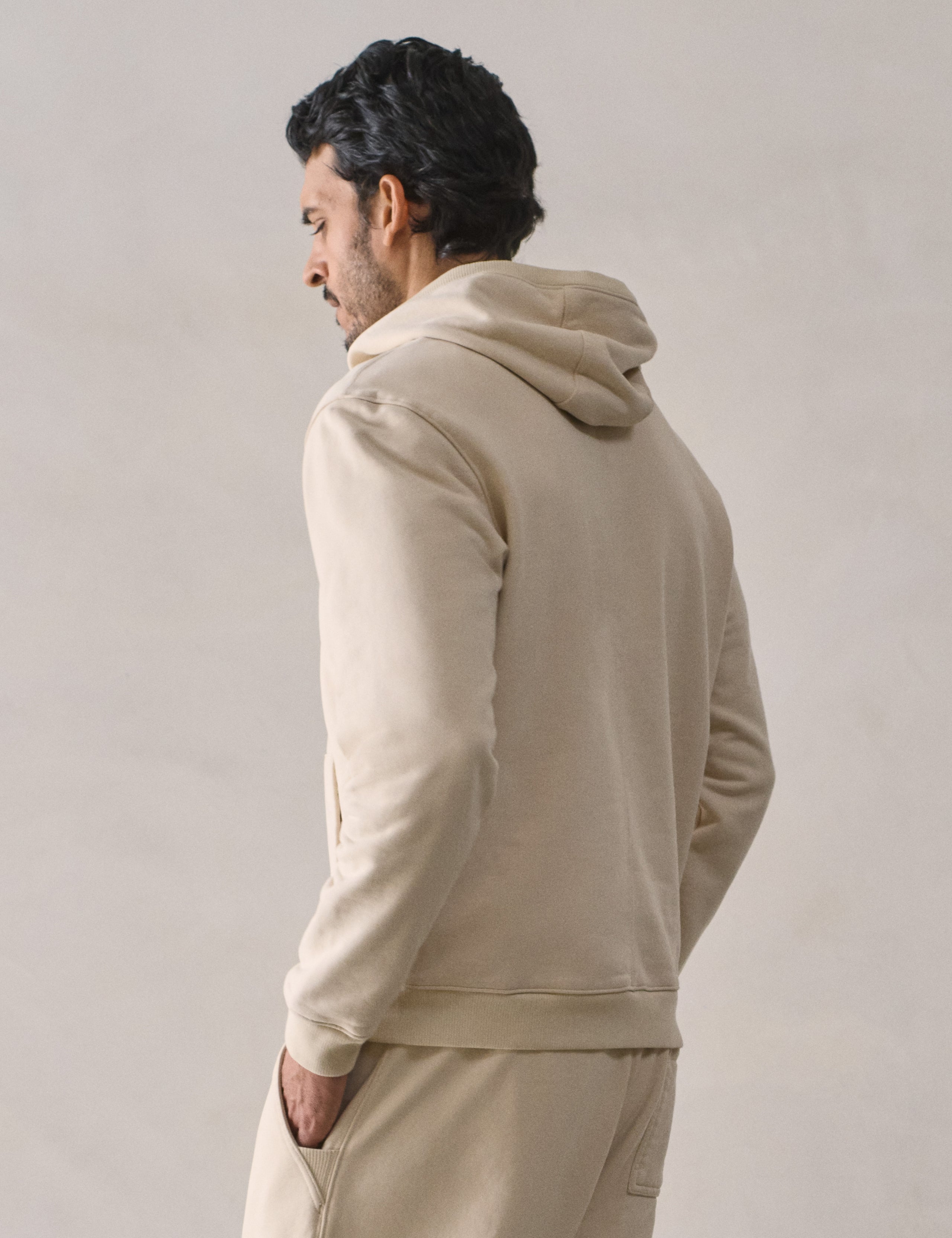 Rear 3/4 upper body view of man wearing Osa Pullover Hoodie in Bone white from AETHER Apparel.