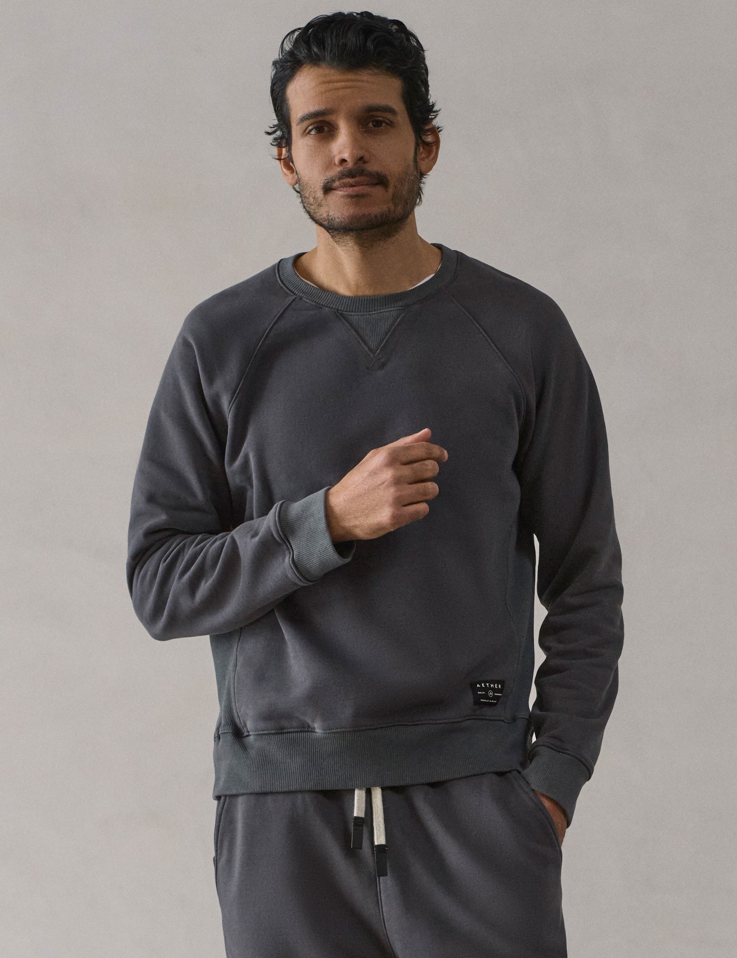 Front upper-body view of man wearing Osa Raglan Sweatshirt in Graphite grey from AETHER Apparel.