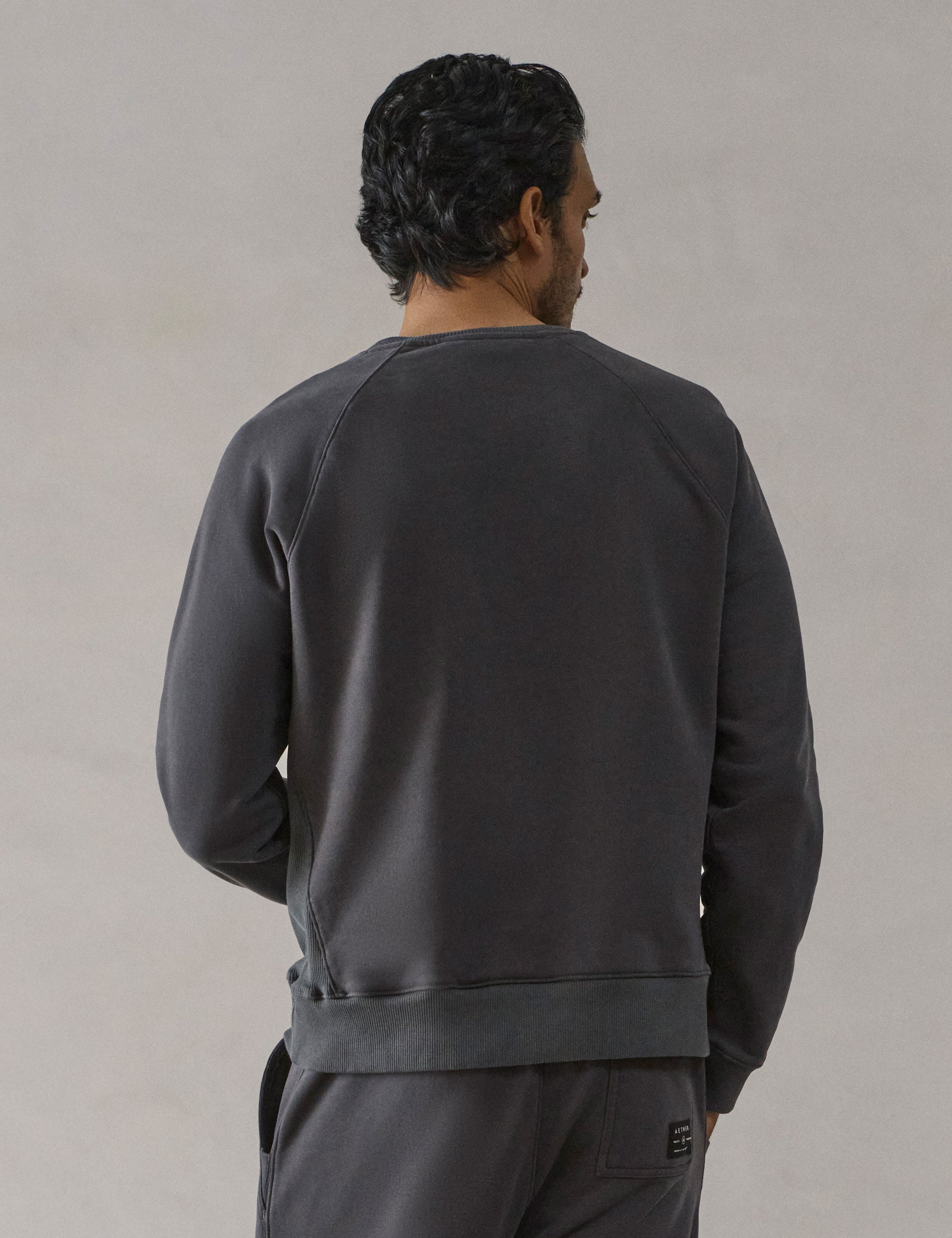 Rear 3/4 full-body view of man wearing Osa Raglan Sweatshirt in Graphite grey from AETHER Apparel.