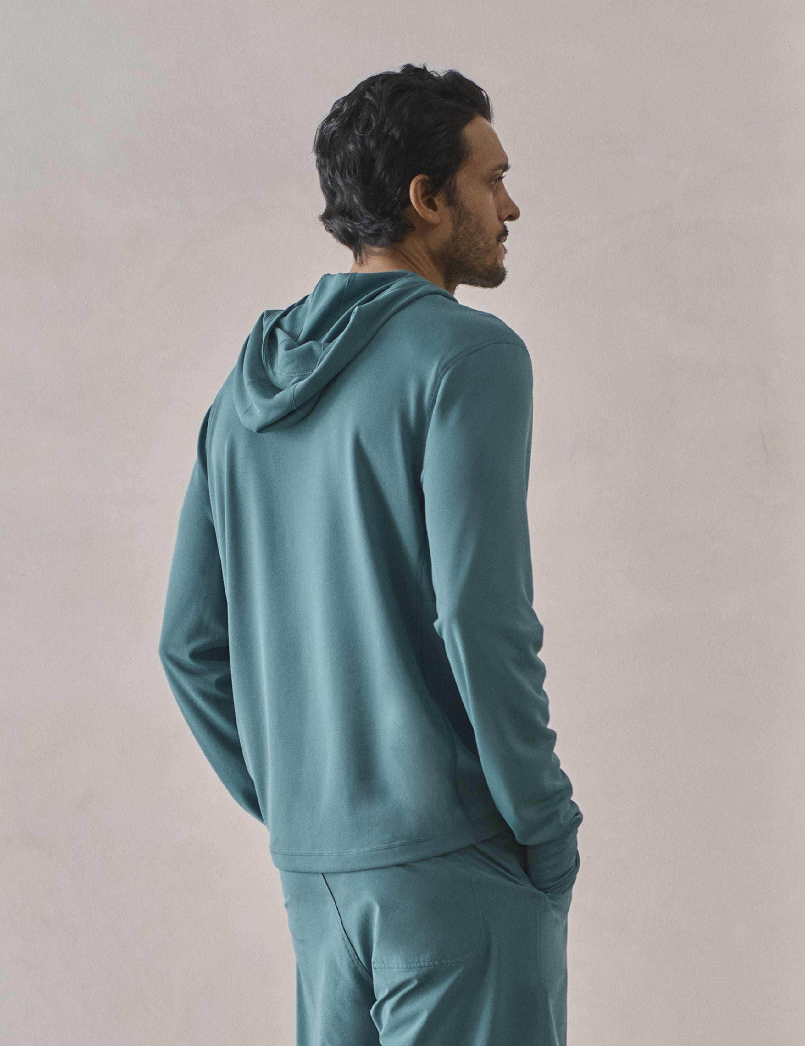 Rear 3/4 upper-body view of man wearing Pacific Hooded Sun Shirt in Aqua Blue from AETHER Apparel.