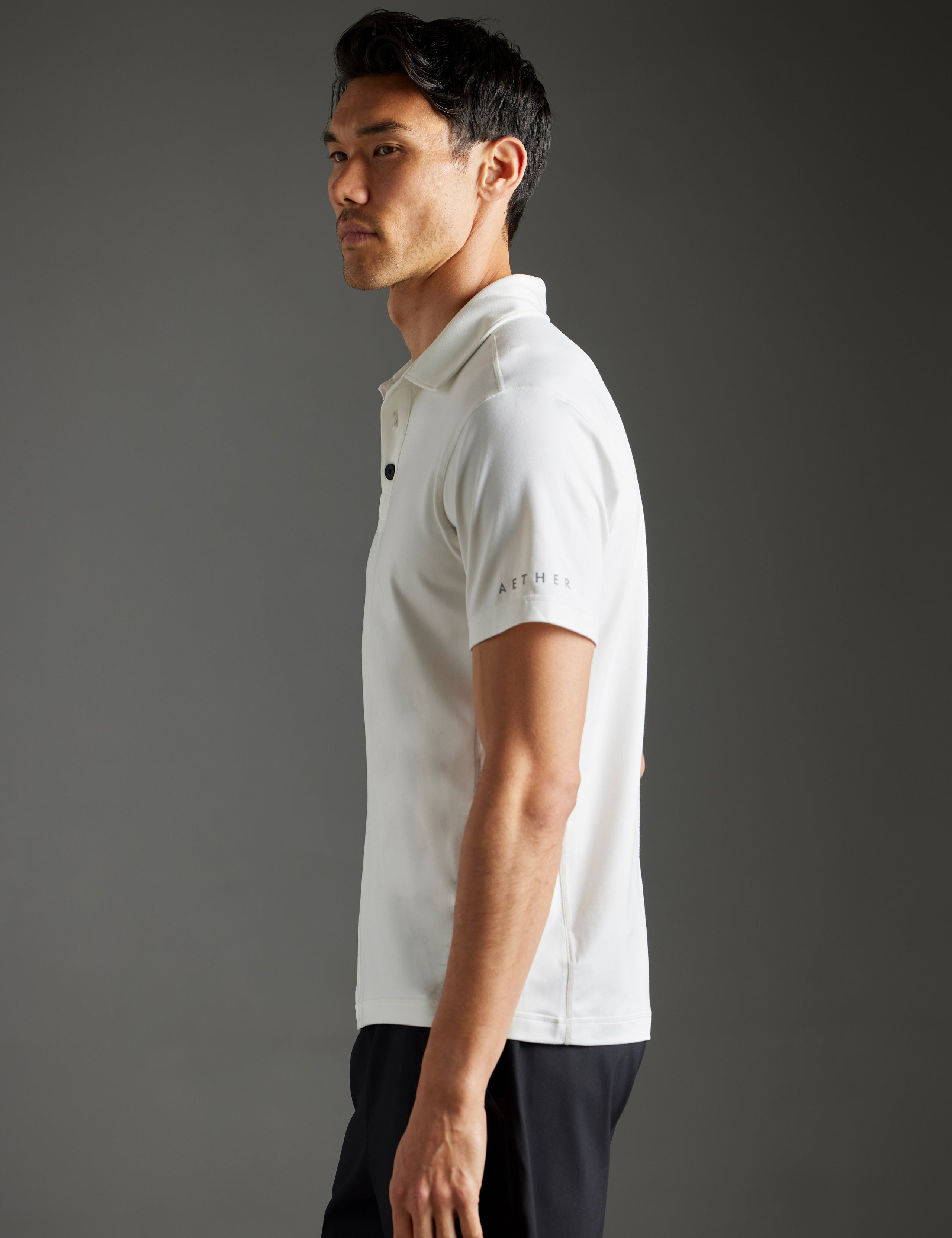 Side profile body view of man wearing Trek Articulated Polo in Natural White from AETHER Apparel.
