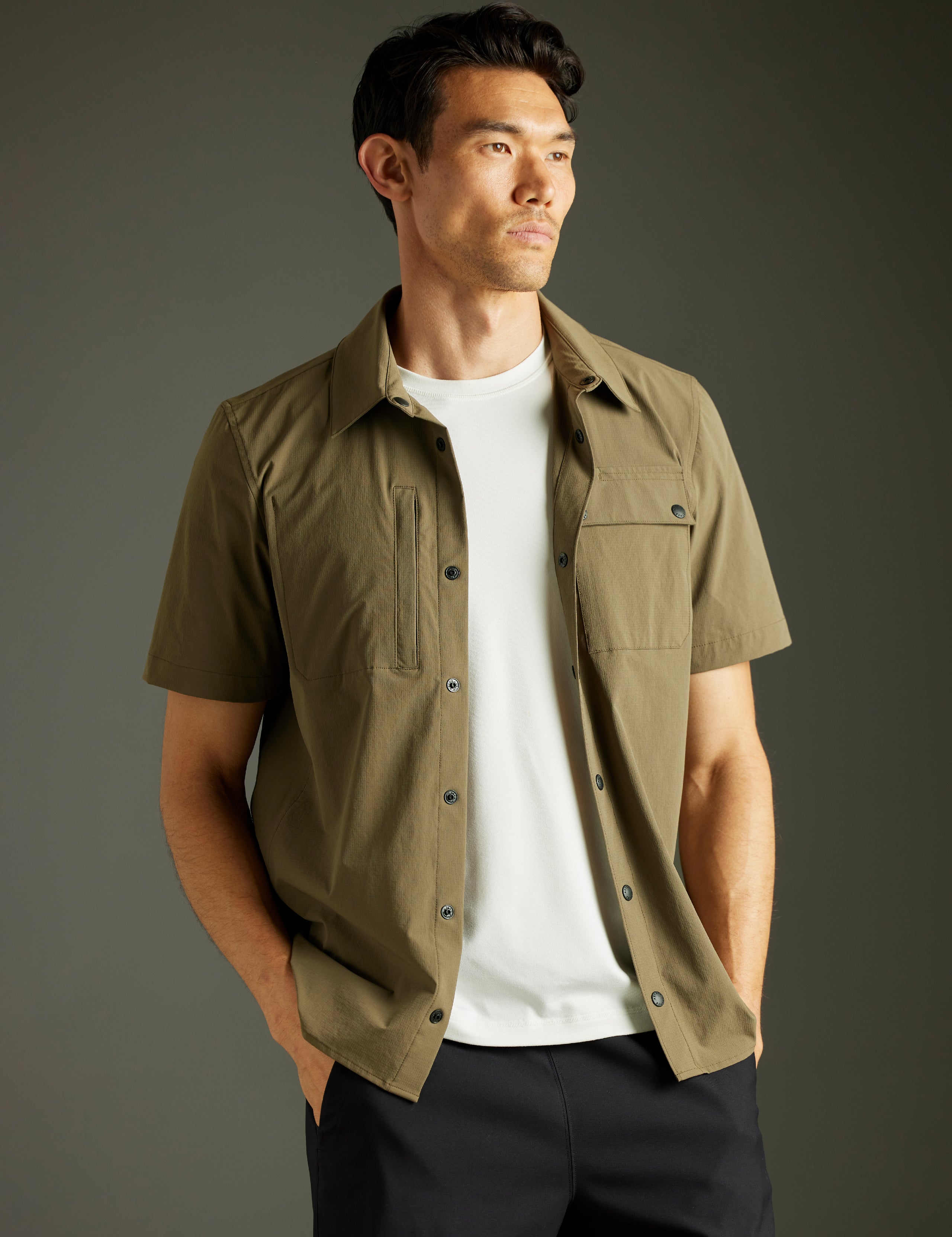 Front 3/4 body view of man wearing unbuttoned Wonder Technical Short-Sleeve Button-Down in Cadet green from AETHER Apparel.