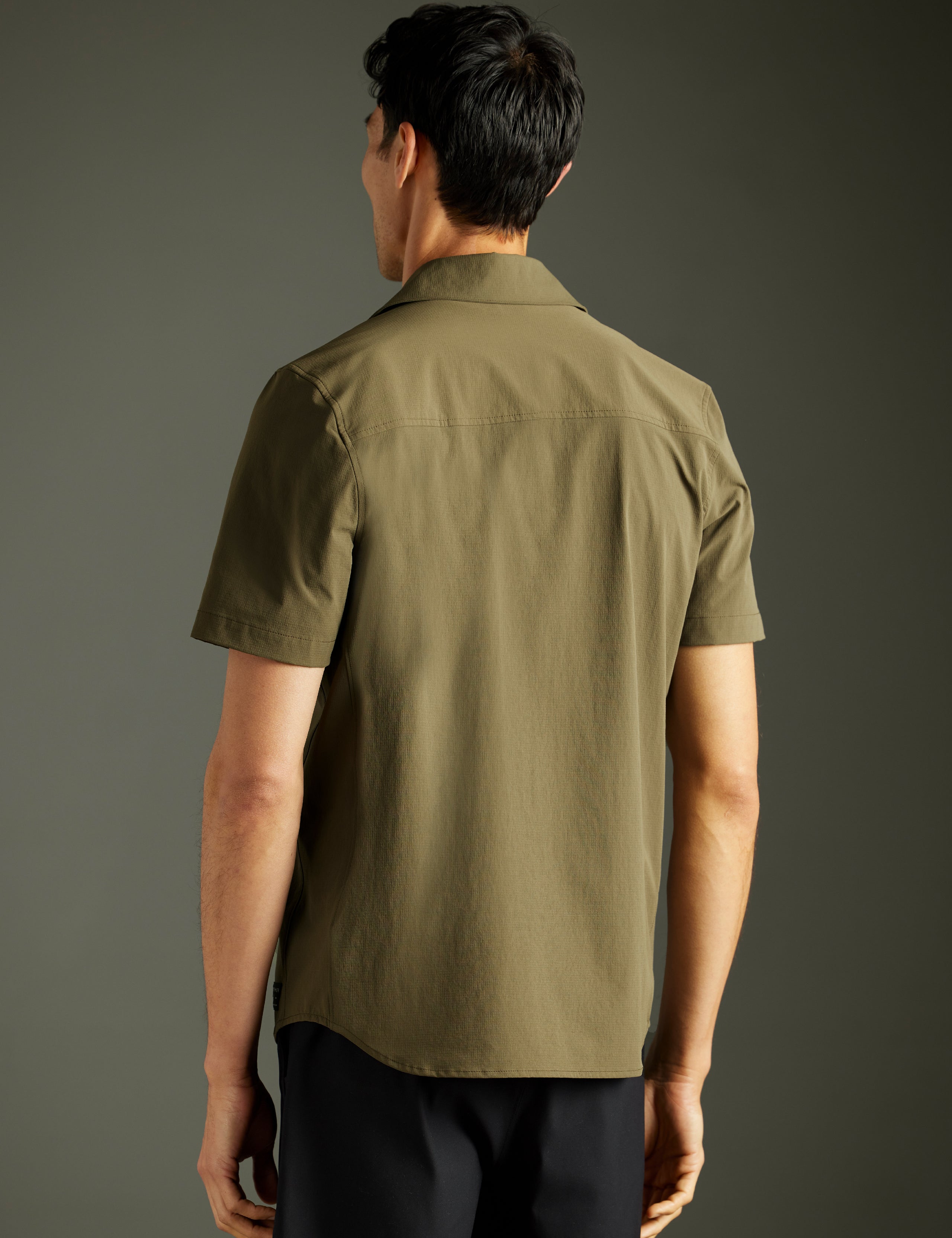 Rear 3/4 body view of man wearing Wonder Technical Short-Sleeve Button-Down in Cadet green from AETHER Apparel.