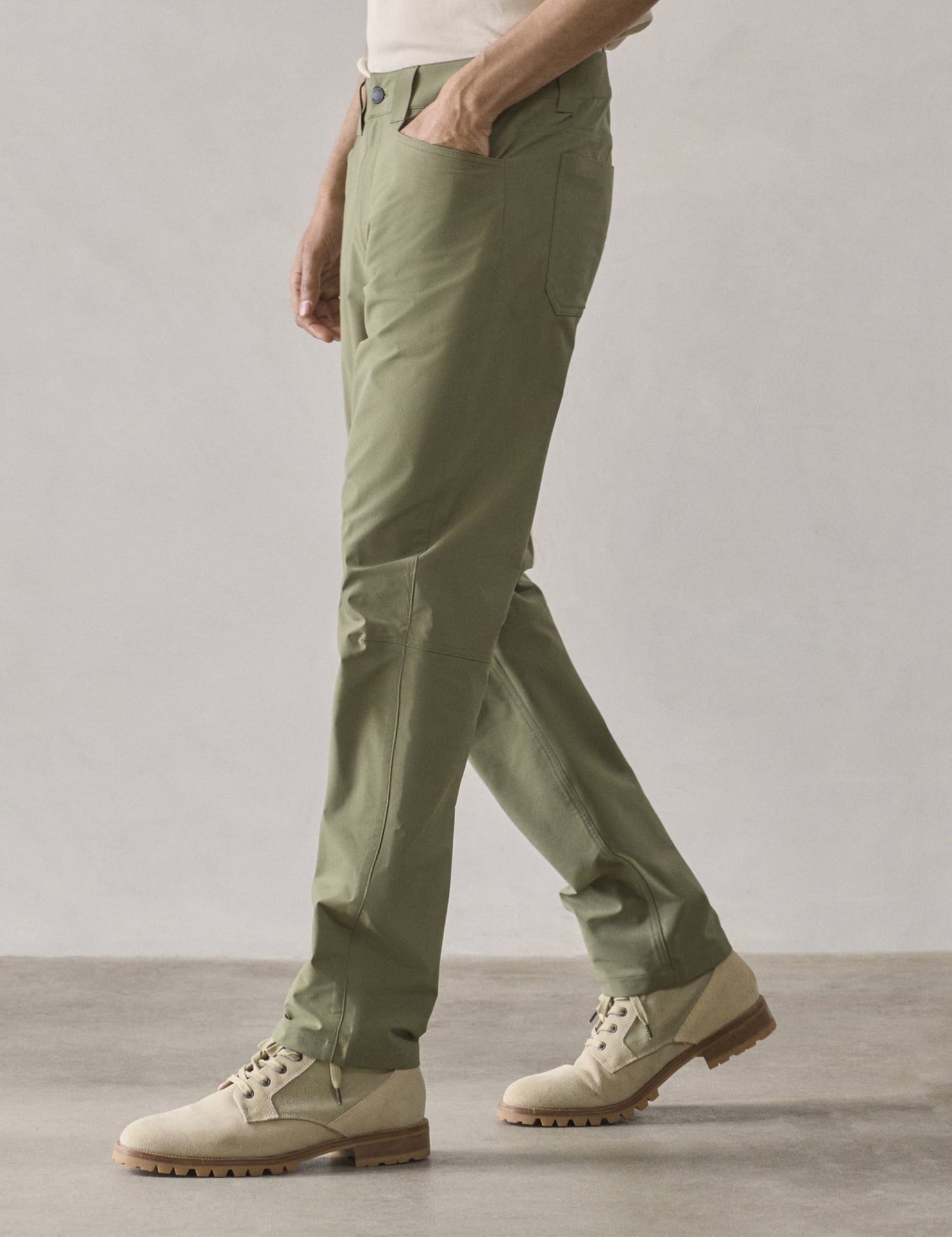 Front 3/4 lower-body view of man walking while wearing Adventure Pant in Fern Green from AETHER Apparel.