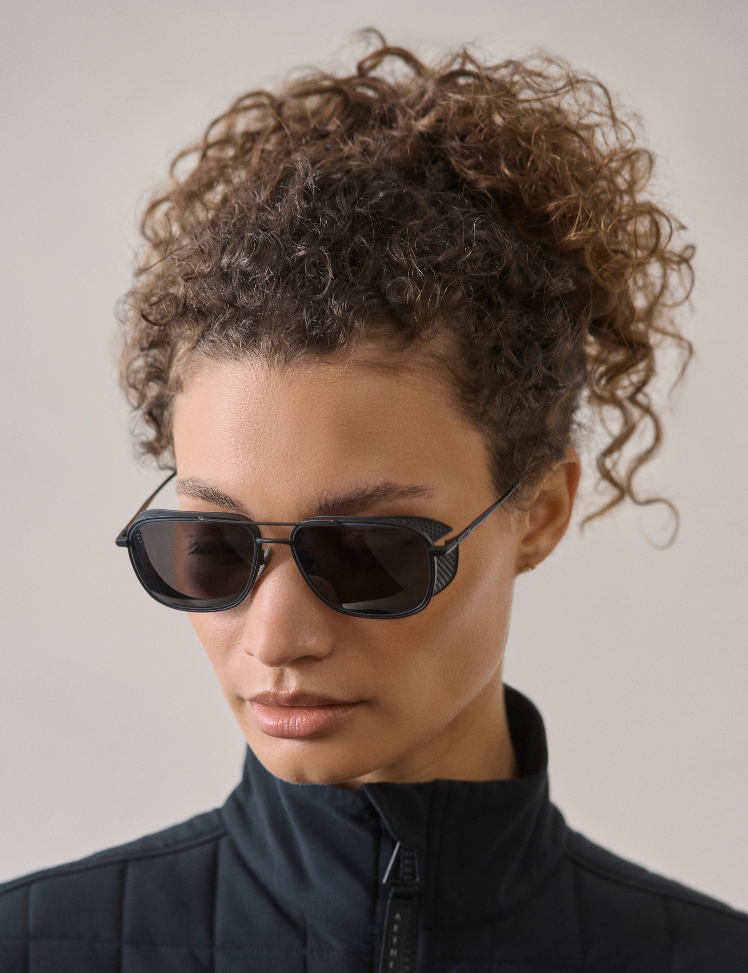 Front 3/4 view of woman wearing Summit Sunglass in Black titanium with black lens from AETHER Apparel.