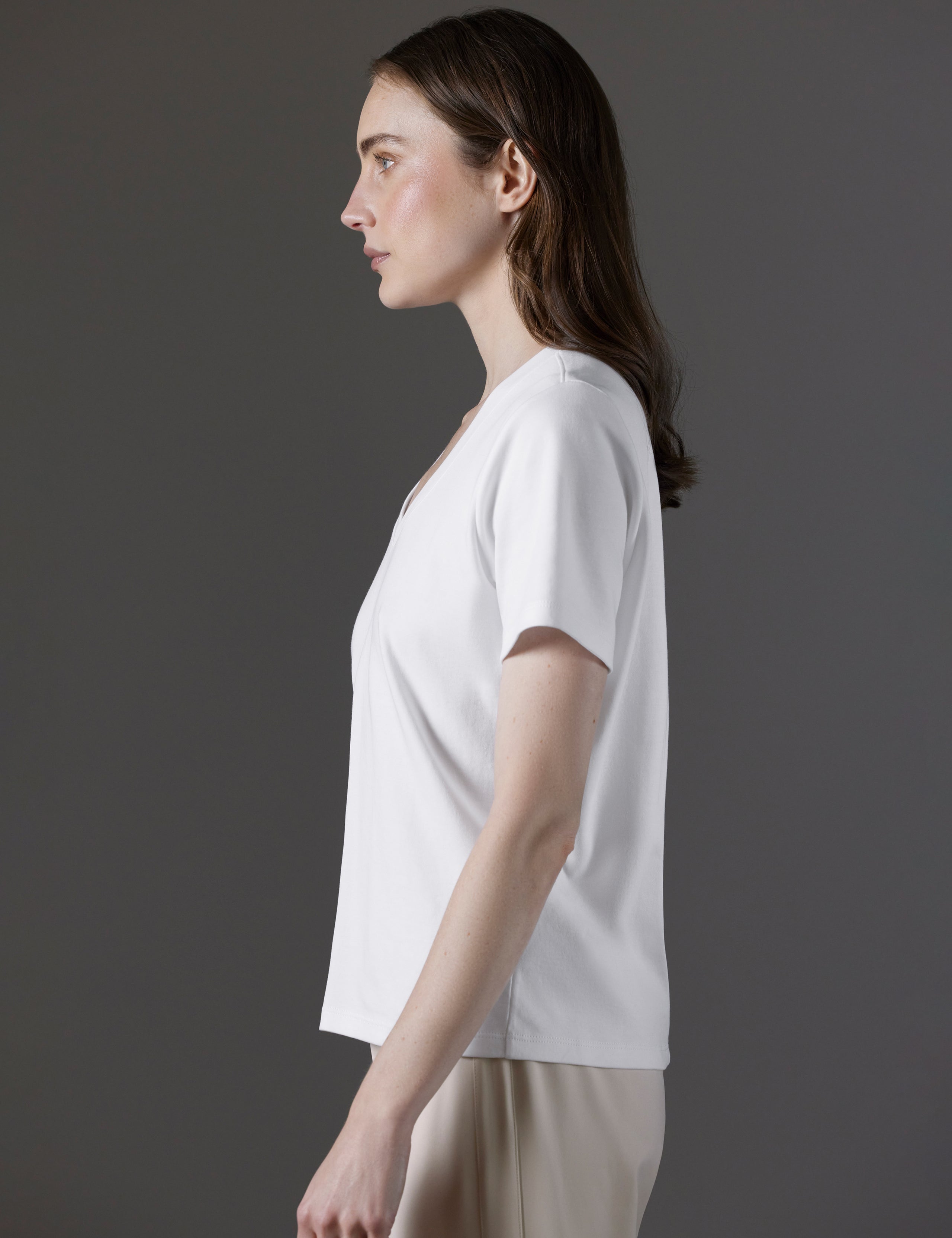 Side profile view of woman wearing Emery Pima V-Neck Tee in White from AETHER Apparel.